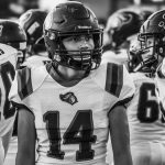 Black and white photo of a high school football team preparing for their game, showcasing teamwork and anticipation.